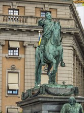 Green statue of a rider on a horse in front of a historic building with impressive architecture,