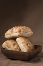 Studio photo of three ciabatta rolls placed in a wooden bowl