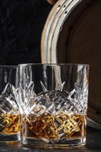 Whiskey in a glass with a barrel. Bourbon whisky and a cask on a dark background, an elegant