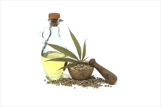 Hemp leaf in front of cannabis oil in glass decanter and hemp seeds isolated on white background.