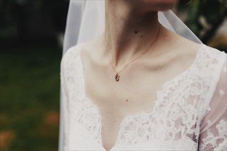 Gold pendant around the neck of the bride in a white dress with veil. Blurred background.