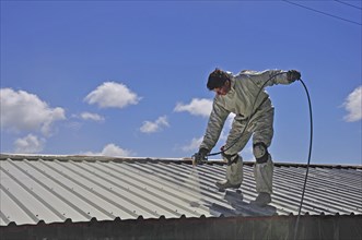 A trademan uses an airless spray to paint the roof of a building