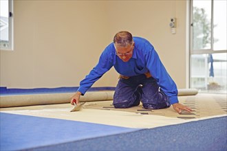 Floorlayer spreading adhesive on the underlay for a carpet laying job