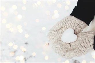 Snow heart snowball in girl gloved hands. Blurred background.