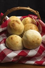 A close up photo of a small basket with a red and white napkin of baked homemade dinner rolls