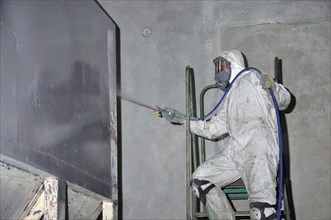 A trademan uses an airless spray to paint a coal hopper inside a manufacturing plant