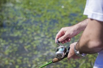 Young man fishing in pond, lake, closeup of fishing rod and reel