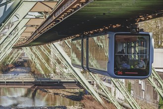 A suspension railway crosses a river in a city, surrounded by architectural metal structures in