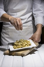 Studio photo of sprinkling parsley flakes on a plate of bowtie pasta