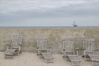 Abandoned deckchairs on the beach in front of a concrete wall with a cruise ship in the background,