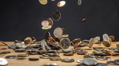 Different coins falling on a wooden table against a dark background