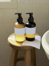 Two pump bottles, one amber and one dark, are placed on a wooden stool, lit by natural light, in a