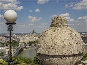 Stone ornament and street lamp with a view of the city and the river under a slightly cloudy sky,