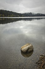 A small boulder is in the calm water of Hauser Lake under a cloudy sky in north Idaho