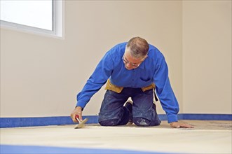 Floorlayer spreading adhesive on the underlay for a carpet laying job