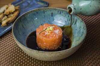 Man turning soy sauce into salmon tartare deliciousness in a beautiful decorated plate