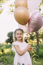 Small shiny girl with pink balloons in the garden.