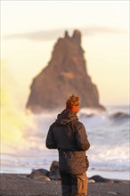 A tourist man with his back turned on the black sand beach of Reynisfjara at sunset in Iceland