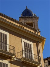 Urban scene with a house and a tower with a blue dome in front of a clear sky, palma de Majorca,