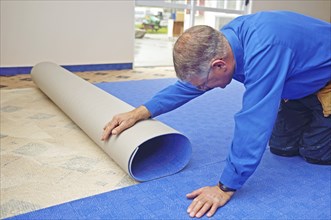 A floorlayer carefully matches the pattern as he rolls out the new carpet