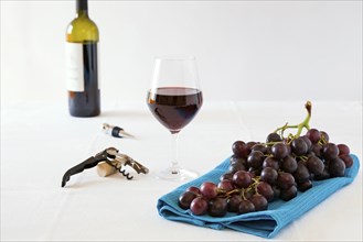 Bunch of red grapes and a glass of red wine with a wine bottle on a white tablecloth