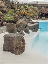 Small part of a pool with blue water, surrounded by large rocks and lush vegetation, lanzarote,