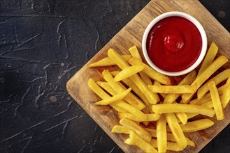 French fries, potato snack with ketchup, fast food on a black stone background, shot from the top