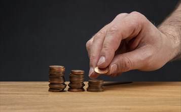 A hand stacking coins on a wooden table against a dark background