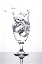 A studio photo of ice being dropped into a glass of water against a white background