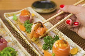 Woman eating delicious gunkan sushi, closeup on chopsticks