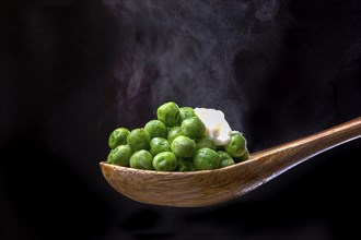 Peas topped with butter on a wooden spoon with steam from below