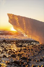 An iceberg with the sun in the background at sunrise on Diamond Beach next to Jokulsarlon in winter