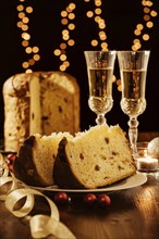 Sliced italian panettone, sparkling wine and decorations with Christmas lights on background