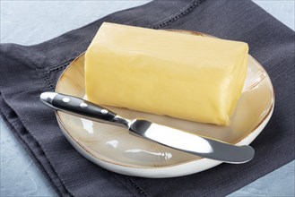 A stick of fresh butter with a knife on a plate, on a slate background, cooking ingredient, Food