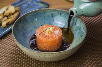 Man turning soy sauce into salmon tartare deliciousness in a beautiful decorated plate