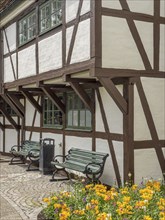 Half-timbered house with white walls and brown wooden beams, planted flower bed and green wooden