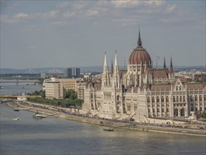 Large historic building on the riverbank with ships on the water and slightly cloudy sky, budapest,