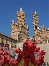 Historic building with gothic towers and a prominent statue in front of red décor on a sunny day,