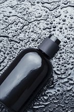 Close-up of a glossy black bottle with water droplets on a textured wet surface, AI generated