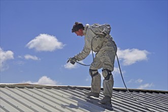 A trademan uses an airless spray to paint the roof of a building