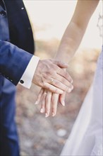 Groom holds bride hand in white dress. Blurred background.