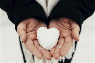 Snow heart snowball in girl gloved hands. Blurred background.