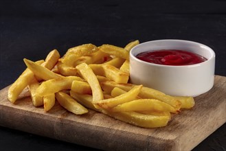 French fries, potato snack with ketchup, fast food on a black slate background, with copy space,