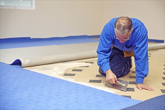 Floorlayer spreading adhesive on the underlay for a carpet laying job