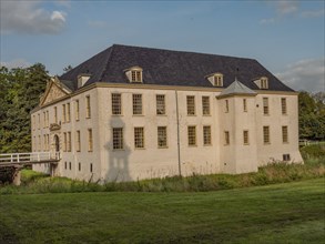 Historic castle with white walls and blue roof, nestled in a large green meadow under a blue sky,