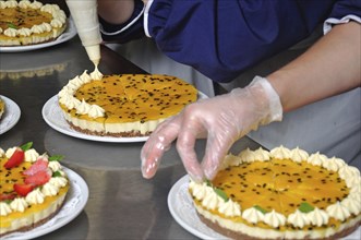 Cook placing cream on the top of a passionfruit cheesecake