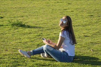 Young woman sitting on the grass, using smartphone on the new Orla do Guaiba in Porto Alegre on