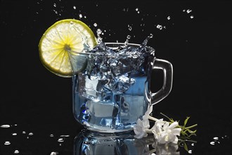 Ice cube splashing into a cup of butterfly pea flower tea with a lime slice