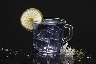 A refreshing glass of cold butterfly pea flower tea with a slice of a lime