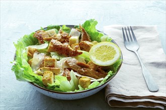 Caesar salad with chicken breast, lettuce, croutons, and a lemon, on a slate background, with a